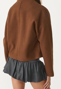 Brązowa krótka kurtka wykonana z wełny, charakteryzująca się prostym wzornictwem, połączona z ciemnoszarym, falbaniastym spódnicą z lekkiego materiału.