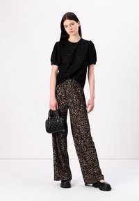 Zwart kortmouwtop met textuurdetails; wijde leopardprintbroek; zwarte geweven handtas; zwarte plateau schoenen.