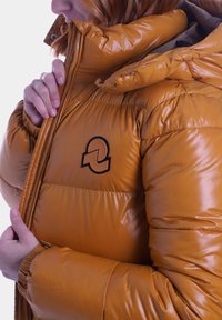 Giubbotto imbottito di un brillante giallo senape con cappuccio. Presenta una patch del logo nera e una cerniera visibile, mostrando una texture trapuntata e un design gonfio.