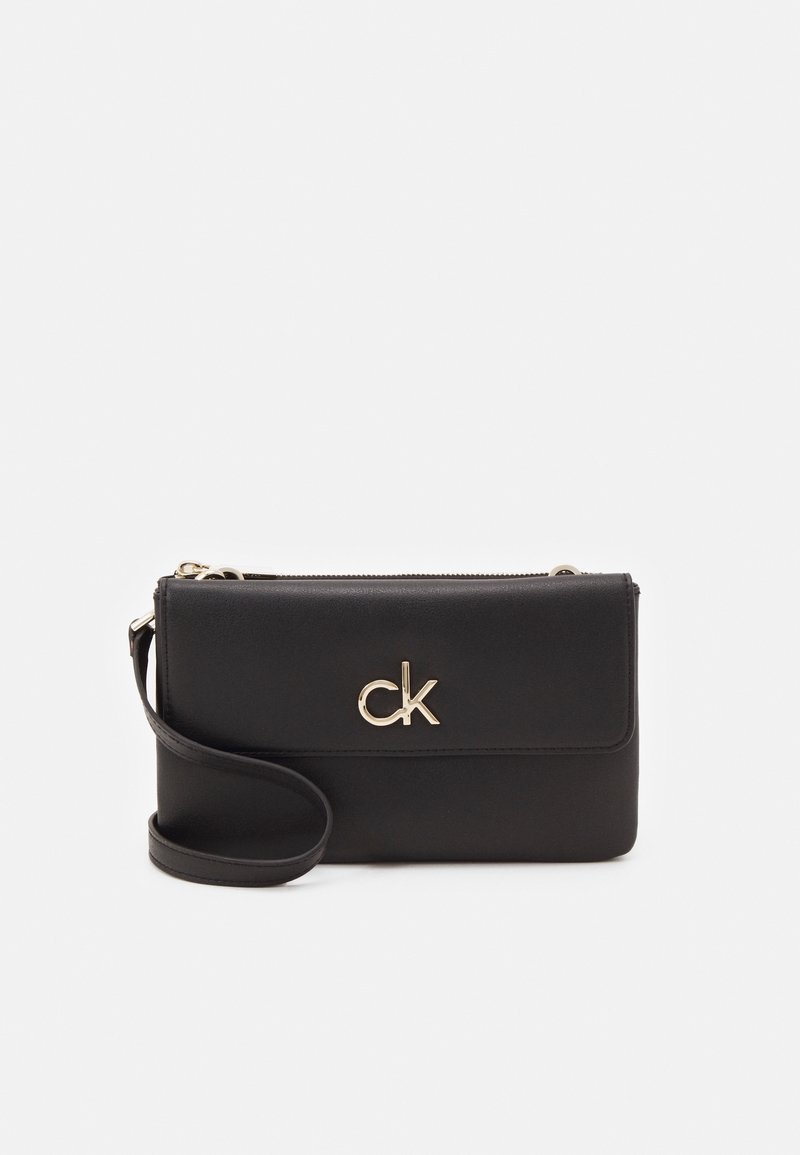 Pochette rectangulaire noire avec fermeture éclair en haut, logo "ck" doré au centre et attache pour le poignet sur le côté gauche.