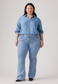 Plava chambray košulja s dugmićima i podvrnutim rukavima, traperice svijetloplave boje s nabranim nogavicama. Nakit je zlatnim dugmićima i detaljima na prednjem džepu.