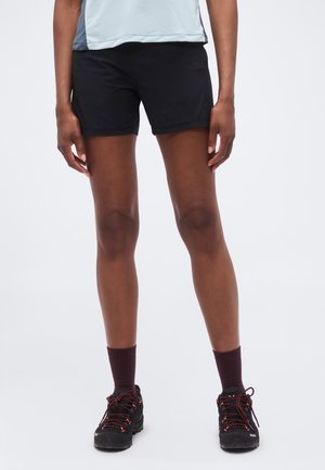 Persoană purtând pantaloni scurți sport negri, șosete bordo închis și pantofi negri de alergare pe trasee cu șireturi roșii, stând pe un fundal alb.