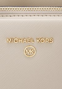 Beżowy portfel ze skórki o fakturze, z złotym zamkiem błyskawicznym, wytłoczonym logo "MICHAEL KORS" oraz okrągłym emblematem "MK" z przodu.