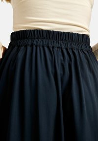 Fekete elasztikus derékszélű szoknya, puha anyagból, begyűrt kialakítással, sima textúrával és áramló sziluettel.