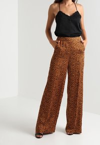 Musta pitsisomistega kampsun, mille juurde on paaritatud laiad leopardimustrilised püksid oranžides ja pruunides toonides, küljetaskudega ning siledast, pehmest materjalist.