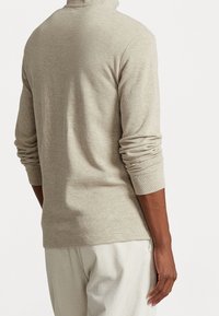 Beige långärmad topp med hög hals. Har ribbad textur och åtsittande ärmslut. Visas bakifrån med en avslappnad silhuett.