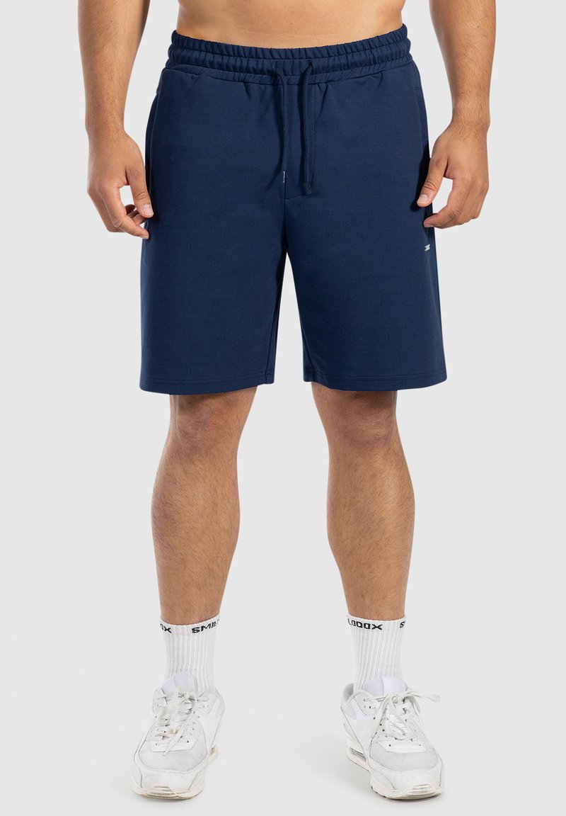 Pantalones cortos deportivos de color azul marino, confeccionados con un tejido suave, que cuentan con una cinturilla elástica y cordón. Alcanzan por encima de la rodilla con un ajuste relajado.