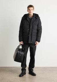Black puffer coat with a hood and front snap buttons, worn over a patterned sweater. Pair of gray jeans and a black leather bag. Black shoes.