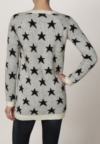 Dzianinowy sweter z szarym tłem, ozdobiony dużymi czarnymi gwiazdami. Rybaczki w białym kolorze oraz dół swetra w kontrastowym wykończeniu. Miękka, fakturowana tkanina.