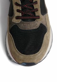 Baskets avec un mélange de maille noire et de daim olive, dotées de lacets rouges et noirs, d'une semelle rembourrée et de subtils accents de couture.