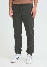 Joggers vert foncé en tissu doux, dotés d'une taille élastique avec un cordon de serrage et des chevilles resserrées. Associés à des baskets blanches.