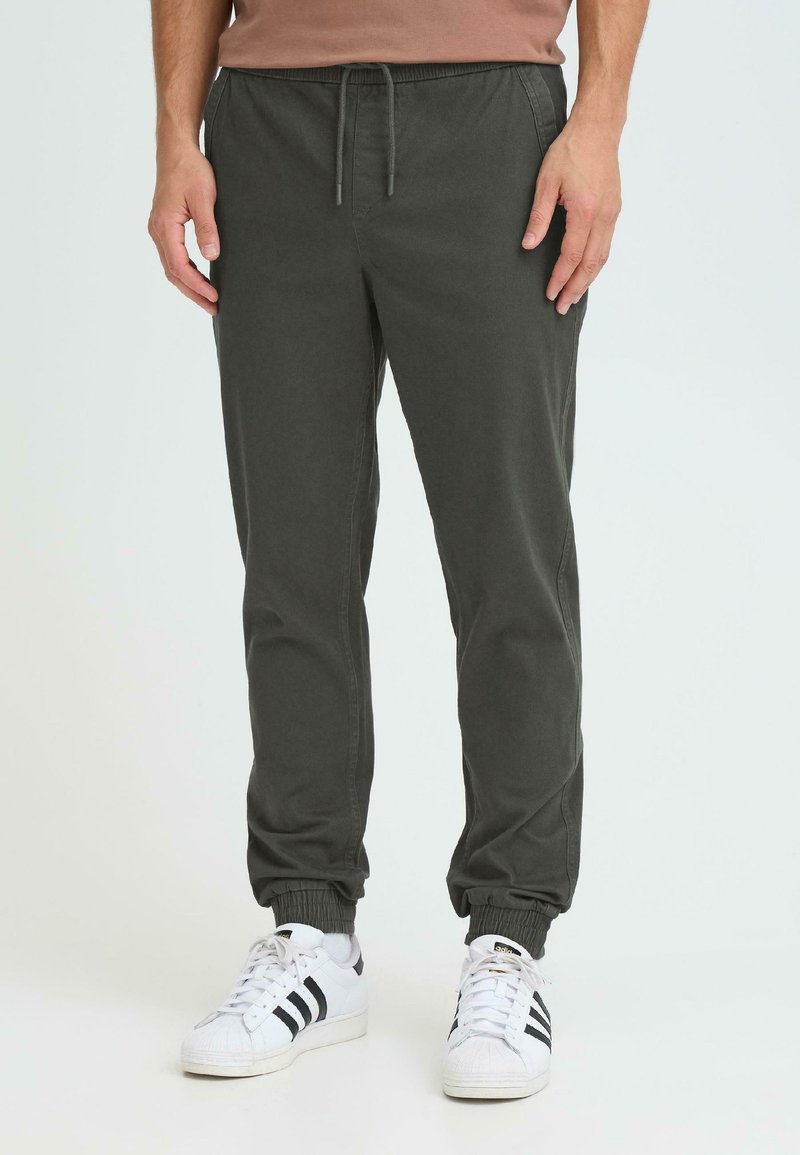 Joggers vert foncé en tissu doux, dotés d'une taille élastique avec un cordon de serrage et des chevilles resserrées. Associés à des baskets blanches.