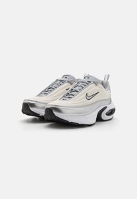 Nike Air tenisky v krémovej a striebornej farbe. Majú štruktúrovaný vrch, okrúlu špičku a odpruženú podrážku s viditeľným vzduchovým vankúšom.