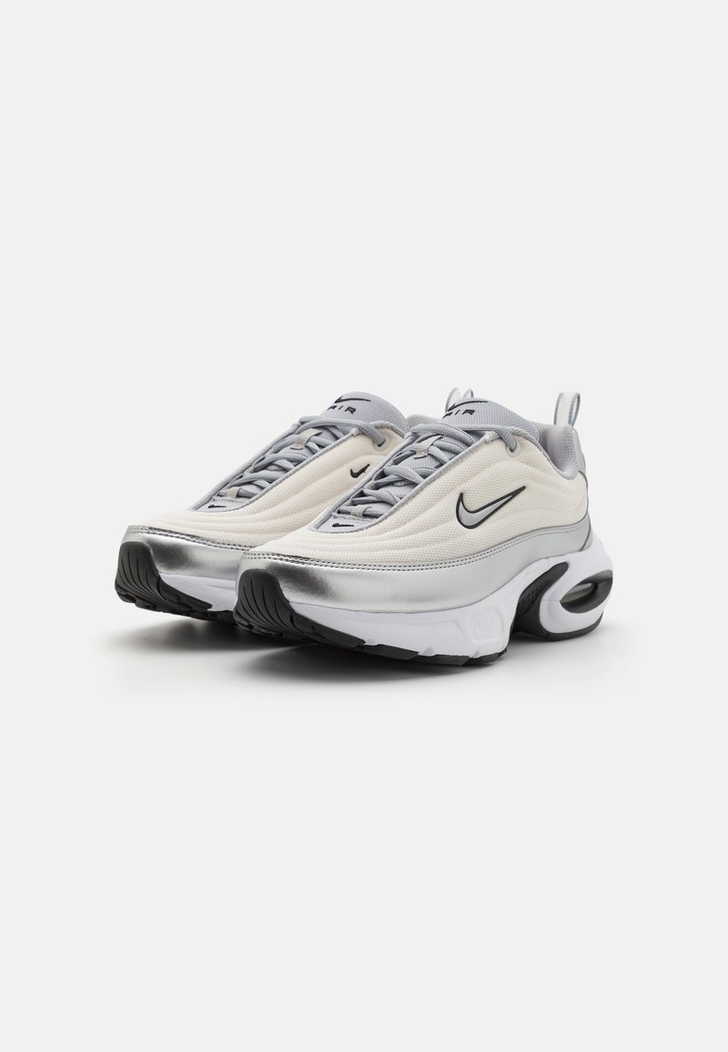 Zapatillas Nike Air en crema y plata. Presentan una parte superior texturizada, puntera redondeada y suela acolchada con amortiguación de aire visible.