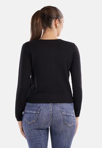 Maglione nero a maniche lunghe con scollo rotondo, design aderente e polsini a coste, abbinato a jeans in denim blu con tasche posteriori.