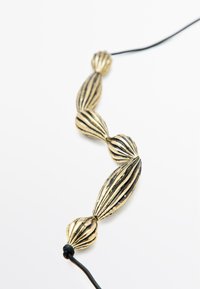 Gouden ketting met gemêleerde, geribbelde kralen van verschillende groottes, geregen aan een zwarte koord. Strak ontwerp en contrasterende kleuren benadrukken de kenmerken.