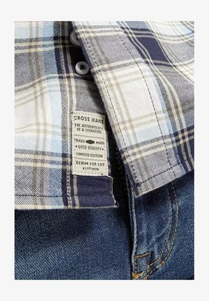 Koszula w kratę w niebieskie, białe i beżowe wzory, z plastikowymi guzikami i metką "CROSS JEANS" wszytą w denimu.