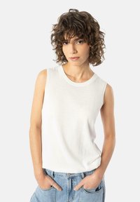 Hvit ermeløs bomullsbluse med rund hals, med en myk tekstur og avslappet passform, kombinert med lyseblå denimshorts.