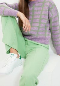 Lawendowy sweter na drutach z zielonym wzorem w kratę, zestawiony z jasnoliwowymi szerokimi spodniami i białymi trampkami z zielonymi akcentami.