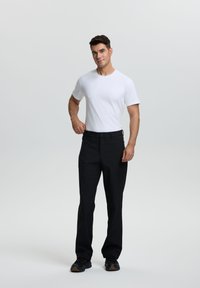 Camiseta blanca de manga corta combinada con pantalones negros. El modelo lleva zapatillas negras. Diseño sencillo, tejido suave y corte relajado.