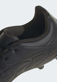 Zapato de fútbol negro hecho de cuero liso, con un collar redondeado, acentos laterales texturizados, cordones planos y un parche con logotipo en el costado.