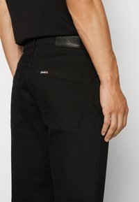 Jean en denim noir au design ajusté, avec une étiquette en cuir à la taille et des poches arrière ornées de coutures discrètes.