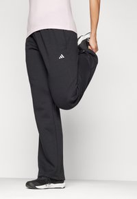 Black athletic pants made of flexible material, featuring an elastic waistband and white logo detail, paired with black sports shoes.