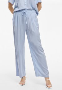 Gaiši zili, vaļīgi bikses, kas izgatavotas no mīksta auduma, ar elastīgu jostu un šnuri, un platām kājām.