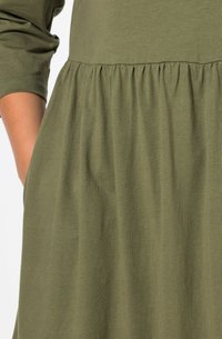 Vestido verde oliva con un torso ajustado y una falda acampanada con detalles fruncidos. Fabricado con una suave tela texturizada.