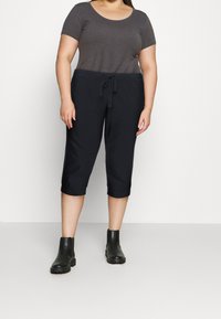 Szary top z krótkim rękawem zestawiony z granatowymi, skróconymi spodniami z sznurkiem w pasie, noszony z czarnymi botkami za kostkę. Gładka, lekka tkanina.