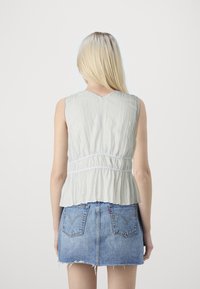 Lys grå ermeløs topp med plisserte teksturer og samlet midje. Kombinert med en blå denim miniskjørt med frynset kant og baklommer.