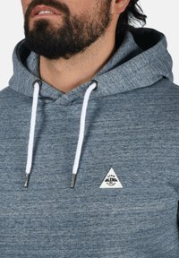 Felpa grigia con cappuccio, caratterizzata da un logo triangolare bianco, con lacci bianchi e occhielli metallici. Texture morbida con un motivo melange.