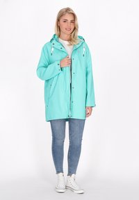 Lengvas mėtų žalios spalvos lietpaltis su kapuce, snap užtrauktukais ir raišteliais. Avimas virš baltos palaidinės ir derinamas su mėlynomis džinsinėmis kelnėmis bei baltomis sportbačiais.