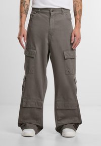 Olivegrüne Cargo-Hose mit lockerer Passform, mehreren seitlichen Taschen und dezenten Nähten. Kombiniert mit weißen Sneakers.