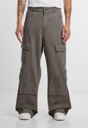Pantalons cargo en vert olive, avec une coupe décontractée, de multiples poches latérales et des détails de couture subtils. Portés avec des baskets blanches.
