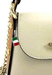 Sac à main en cuir beige avec une bandoulière en chaîne dorée et un petit pendentif représentant le drapeau italien attaché à la fermeture éclair, doté d'une texture lisse et de quincaillerie polie.