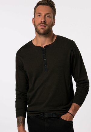 Dunkelbraunes Langarmshirt mit einem gerippten Muster, das einen runden Ausschnitt und eine Knopfleiste mit vier Knöpfen aufweist. Getragen mit schwarzen Hosen.