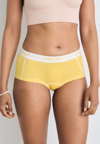 Žute pamučne bokserice za dječake s bijelom waistband oznakom "PIECES." Imaju kontrastne šavove i glatku teksturu.