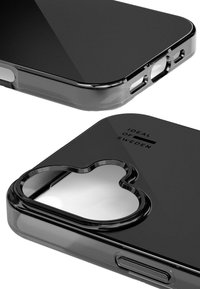 Coque de téléphone noire transparente avec une découpée en forme de cœur pour l'objectif, texture lisse et logo en relief sur la surface. Les ouvertures pour les ports sont visibles.