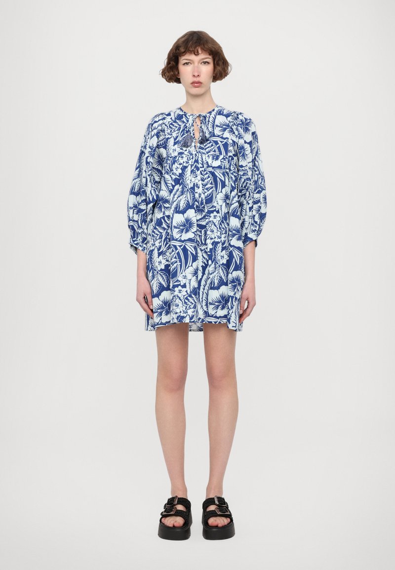 Blauw jurk met bloemenprint, met een ontspannen pasvorm, pofmouwen en striknek, met witte hibiscus en bladenpatronen. Gecombineerd met zwarte platform sandalen.