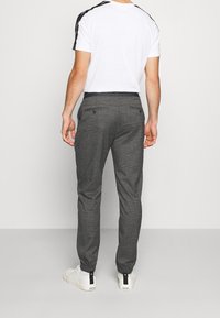 Grå mönstrade joggers med elastisk midja och fållade anklar, kombinerade med en vit t-shirt och vita sneakers.