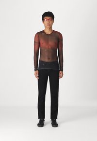 Camisola preta de malha de mangas longas com textura transparente, combinada com jeans pretos e ténis pretos. O modelo usa óculos de sol vermelhos. Fundo simples.