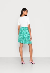 Top branco canelado de manga curta combinado com uma saia verde com flores. A modelo usa sapatos de salto abertos rosa. Vista traseira destacando o contraste de tecidos e cores.