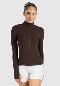 Bruine ritsjack met hoge kraag, lange mouwen en twee zijzakken. Gladde textuur met een figuurvolgend fit, met subtiele stikdetails.