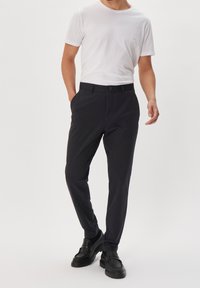 Donkergrijze broek met een slim fit, zijzakken, een enkele knoopsluiting en een gladde stoftextuur, gecombineerd met een effen wit T-shirt.