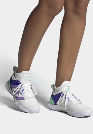 Zapatillas deportivas blancas con acentos morados y verdes, que cuentan con un upper de malla texturizada, diseño de cordones y un collarín acolchado en el tobillo.