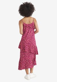 Lila Blumenkleid mit Rüscheträgern und mehrlagigem Saum, aus leichtem Stoff, getragen mit weißen Sneakers. Rückansicht gezeigt.