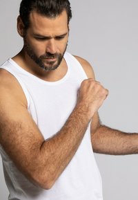 Weißes Baumwoll-Tanktop, das von einem Mann getragen wird, mit Rundhalsausschnitt und weiten Armausschnitten, sichtbaren Nähten und einer glatten Textur.