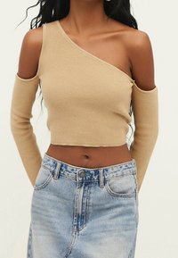 Beige geribbelde crop top met een schouder uitsnede en lange mouwen, gecombineerd met een lichtblauwe denim rok met een knoop en zakken.