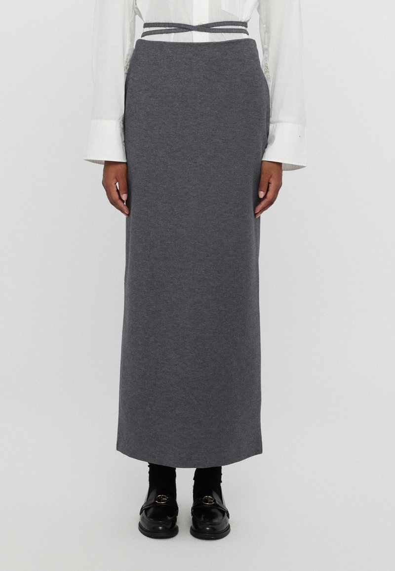 Falda gris hasta la rodilla hecha de una tela suave, con una cintura ajustada y un cinturón texturizado. Combinada con mocasines negros y calcetines negros.
